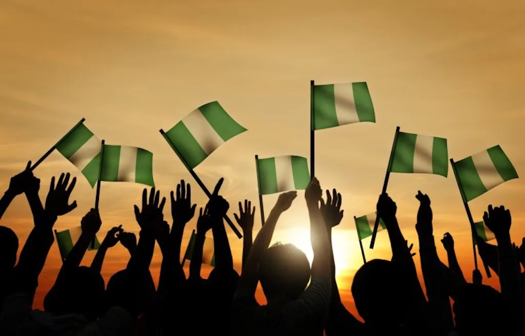 Silhouettes of hands raising Nigerian flags high against a sunset sky